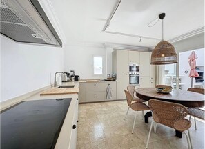A modern kitchen with a dining area, including a round table and wicker chairs, a built-in oven, and a hanging light fixture. - Mb.b53 - Beachfront Penthouse With Sea Views (Estepona)