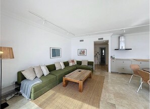 A living room with a green sofa, a wooden coffee table, and a kitchen area with cabinets and a stove. - Mb.b53 - Beachfront Penthouse With Sea Views (Estepona)