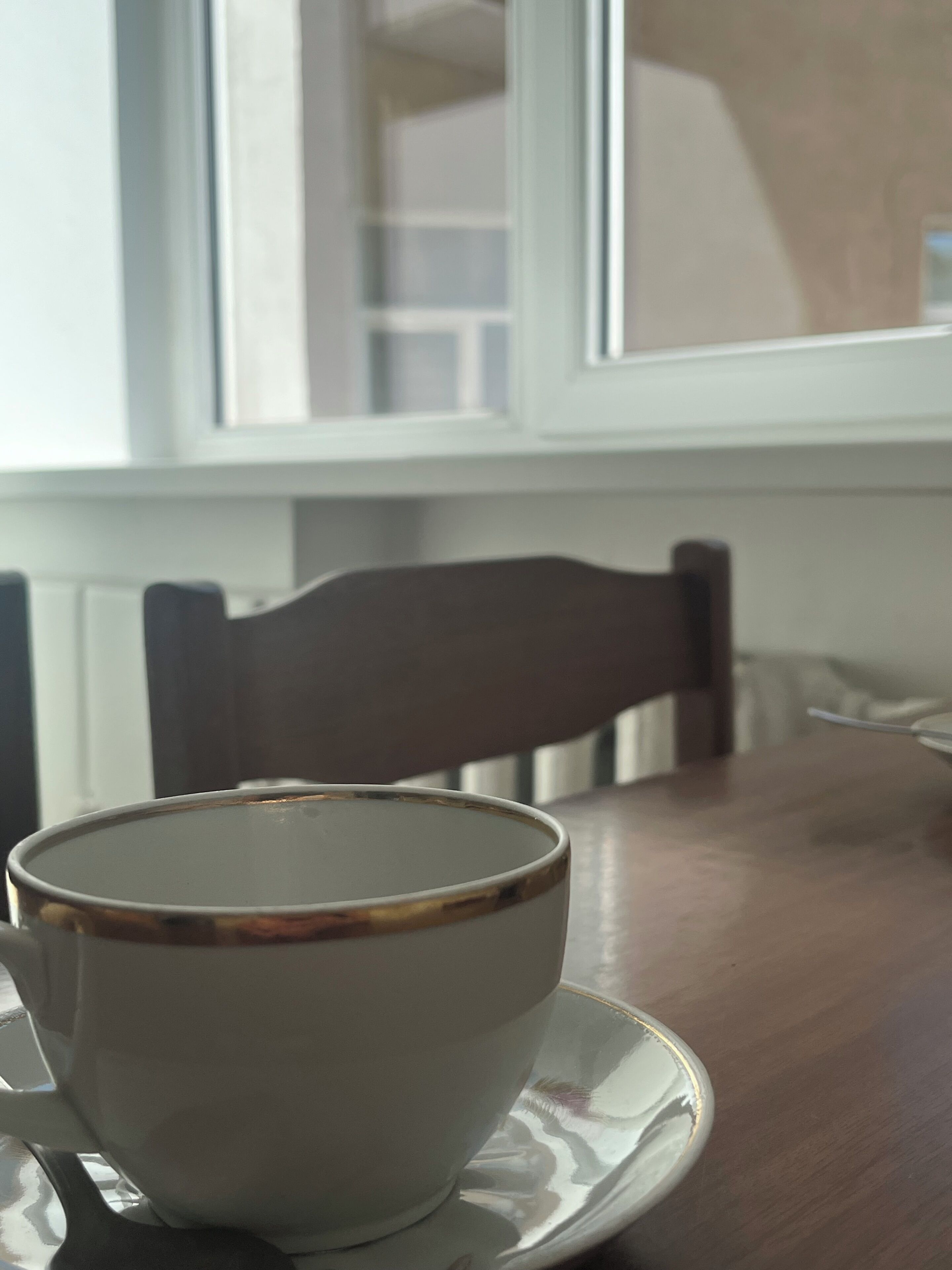 A cup on a saucer on a table with a chair in the background.