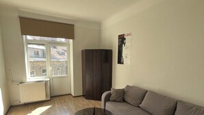 A living room with a sofa, a glass coffee table, a radiator, a window with blinds, and a poster on the wall.