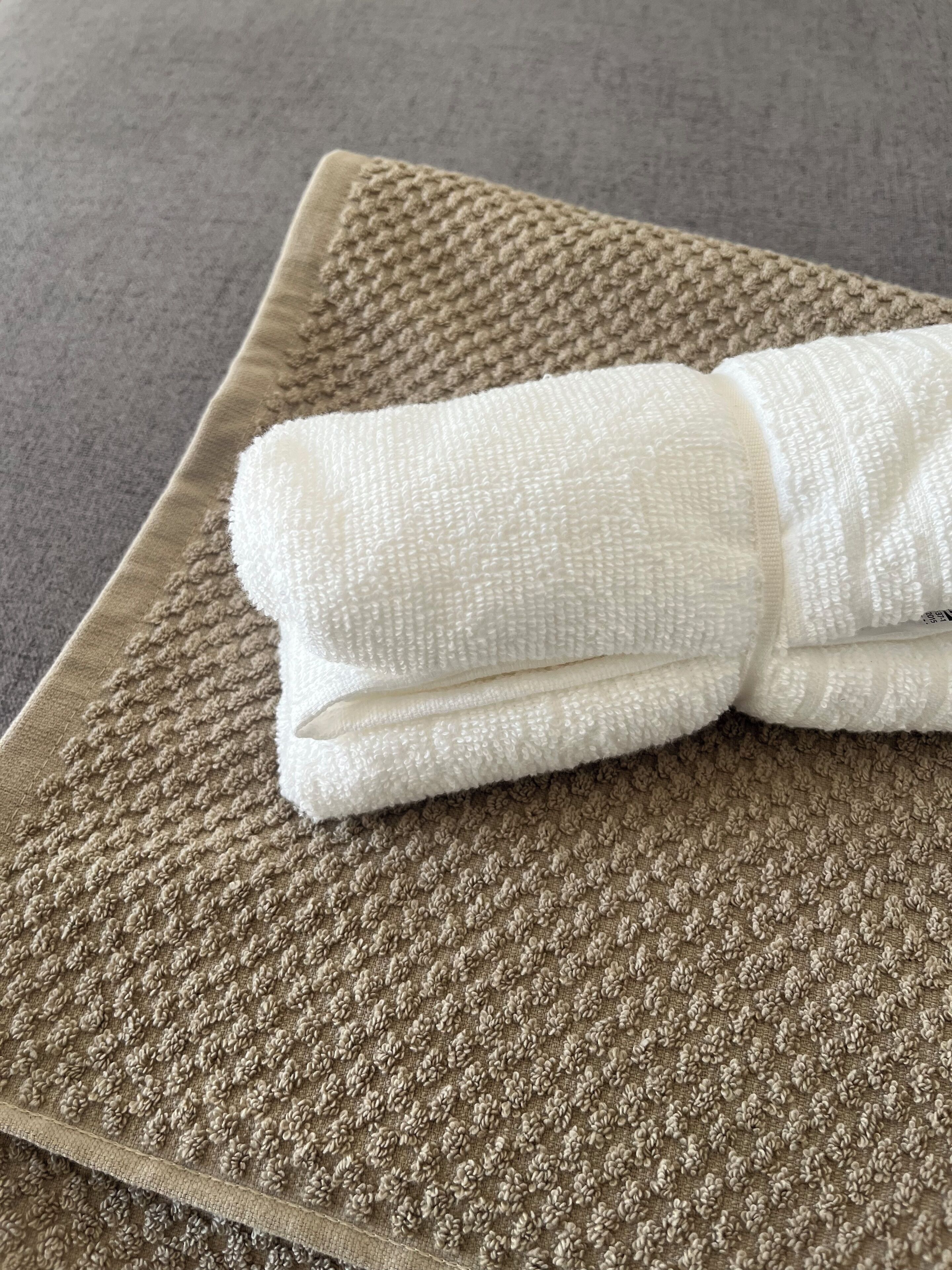 Une serviette blanche, soigneusement pliée, est posée sur un tapis beige à texture.
