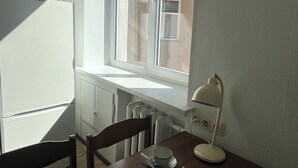 A kitchen with a window, a table with chairs, a refrigerator, and a lamp.
