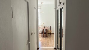 A hallway leading to a dining area with a table and chairs, a door on the left, and a sliding glass door on the right.