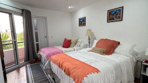 Une chambre avec deux lits, une fenêtre avec des rideaux, une porte, une lampe et deux tableaux accrochés au mur.