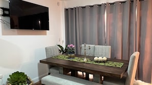 Un espace repas comprenant une table, des chaises, un banc, un téléviseur fixé au mur et un rideau.