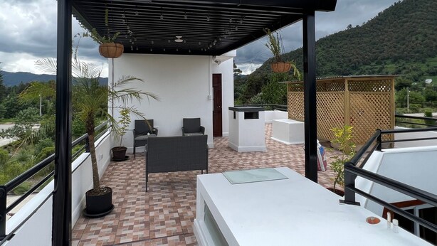 Une terrasse sur le toit dotée d’un espace salon couvert, de plantes en pot et offrant une vue sur le paysage environnant.