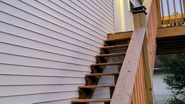 A wooden staircase leading to a house with white siding and a visible window.