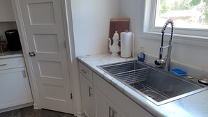 A kitchen with a built-in dishwasher, a sink with a faucet, a window, and a door leading to another room.