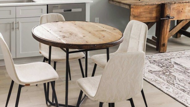 Een eetgedeelte met een ronde houten tafel en vier stoelen, een keuken met witte kasten, en een televisie op een houten dressoir.