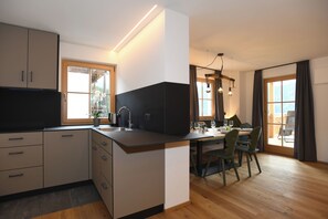 A modern kitchen with a dining area, wooden flooring, and large windows. - "Tesitten" | ZumMoarSepp - Holiday apartment in the Villnöss Valley (Trentino-Alto Adige)