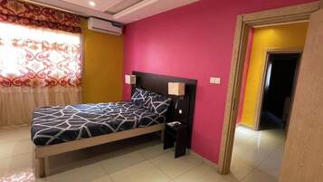 A bedroom with a bed, bedside tables, a nightstand, a window with curtains, and a door.