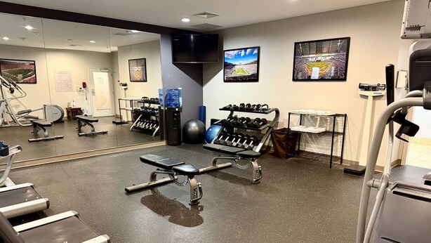 A gym with exercise equipment, a mirror, and a television displaying a sports event. - Accessible 1BR Suite | Pool & Daily Breakfast (Oconomowoc)
