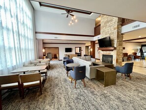 A hotel lobby with a seating area, a fireplace, a flat-screen TV, and a staircase leading to an upper level.