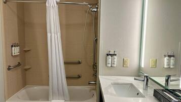 A bathroom with a bathtub, a shower, a vanity with a mirror, and toiletries on the wall.