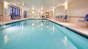 A large indoor swimming pool with clear blue water, surrounded by lounge chairs and a tiled wall.