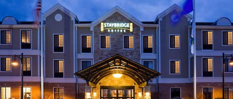 A Staybridge Suites hotel with a brick facade, a central entrance with a covered porch, and a flagpole with an American flag.