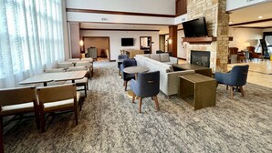 A hotel lobby with a seating area, a fireplace, a flat-screen TV, and a staircase leading to an upper level.