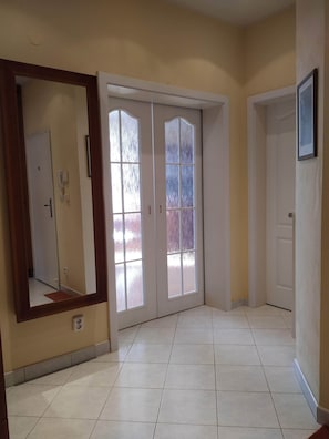 Un pasillo con un espejo grande, puertas dobles y piso de baldosas.