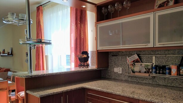 Una cocina con encimeras de granito, armarios de madera, una cava y una ventana con cortinas.