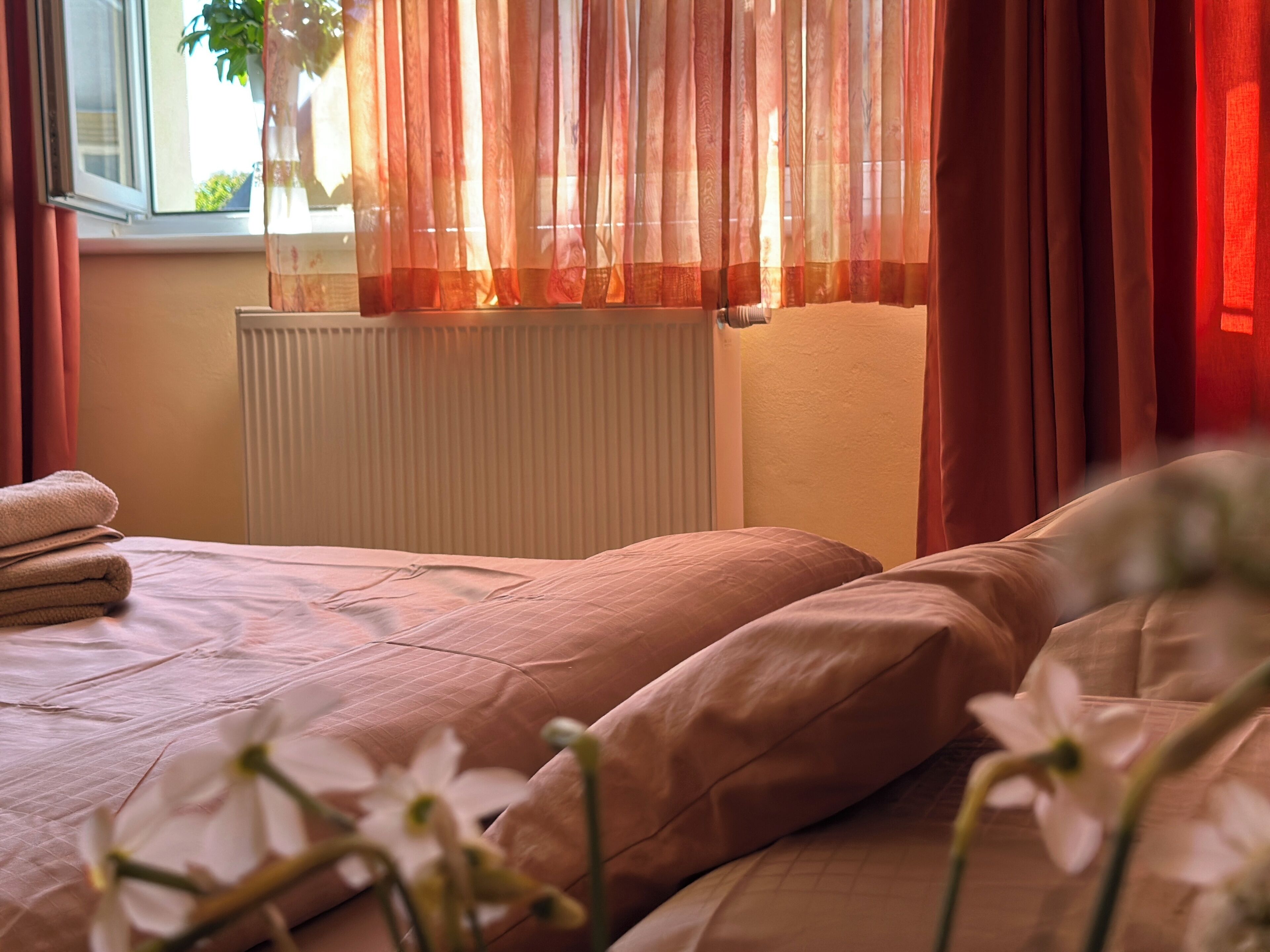 A bed with a white bedspread, a radiator, and red curtains.
