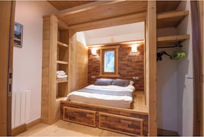 Camera da letto con struttura in legno, un letto, mensole a parete, una finestra e un termosifone.