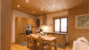 A wooden interior with a dining table set for four, a kitchen with a stove and oven, and a window with a view. - Chalet-like triplex with separate entrance ideal for large families (Les Contamines-Montjoie)