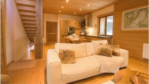 A cozy living room with a white sofa, wooden ceiling, and a kitchen in the background. - Chalet-like triplex with separate entrance ideal for large families (Les Contamines-Montjoie)