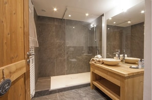 Un bagno moderno con doccia, un mobile bagno in legno e uno specchio grande.