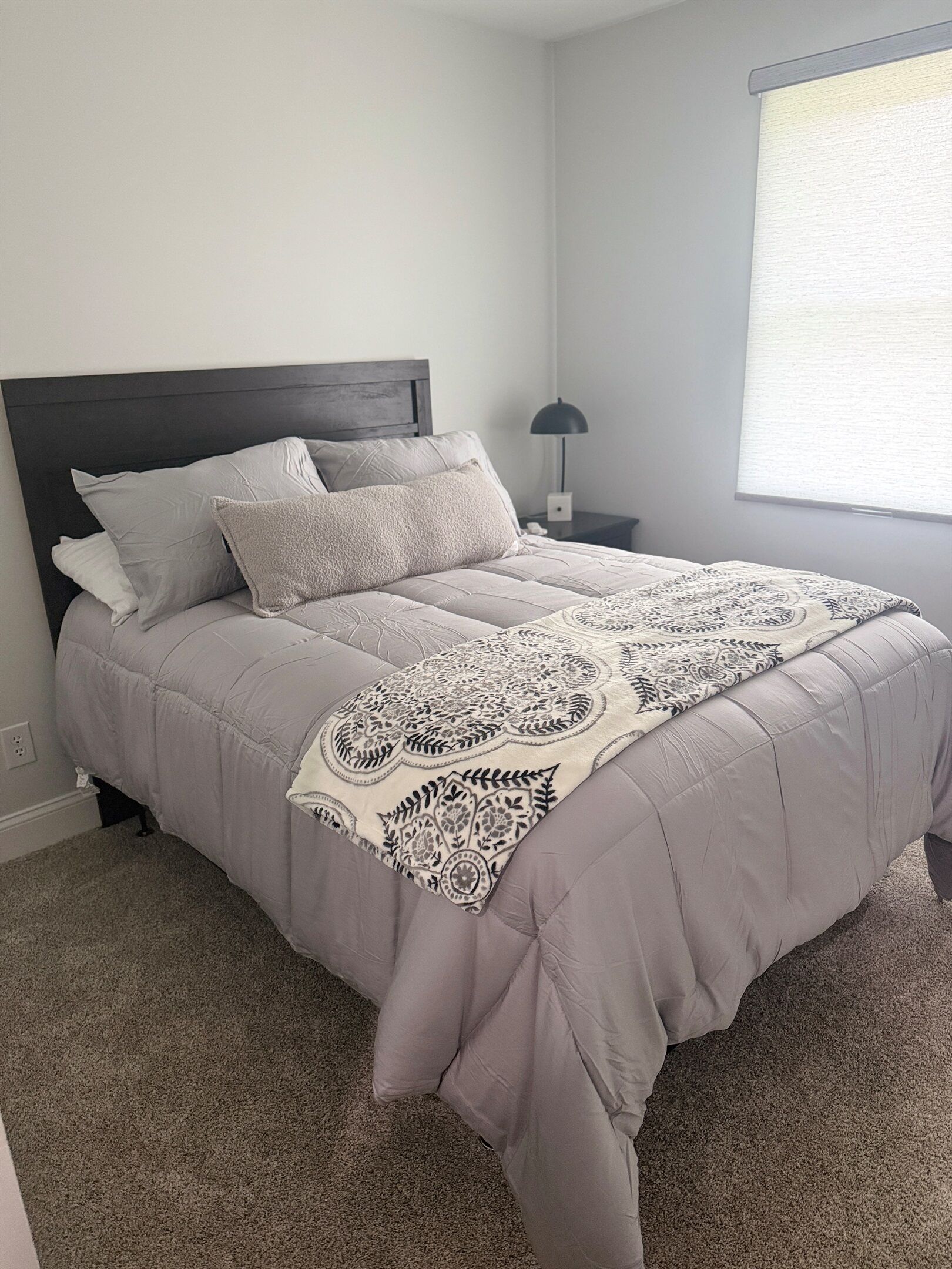 A bed with a patterned throw, a dark headboard, and a bedside lamp.