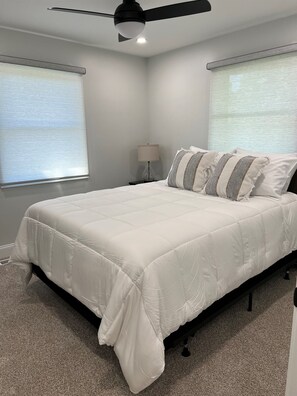 A bedroom with a bed, a ceiling fan, a nightstand with a lamp, and two windows with blinds. - Harrison Place - Located on Evansville's Eastside (Evansville)