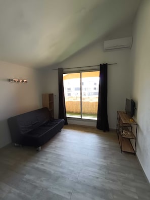 Ein Zimmer mit einer schwarzen Couch, einem Holzboden-TV-Schrank und einem großen Fenster mit Vorhängen.
