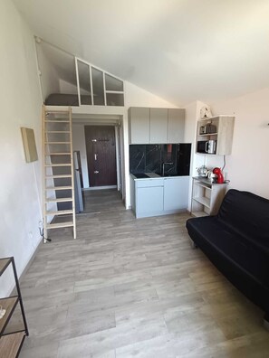 Ein kompakter Wohnraum mit Schlafgalerie, Küchenzeile und einer schwarzen Couch.