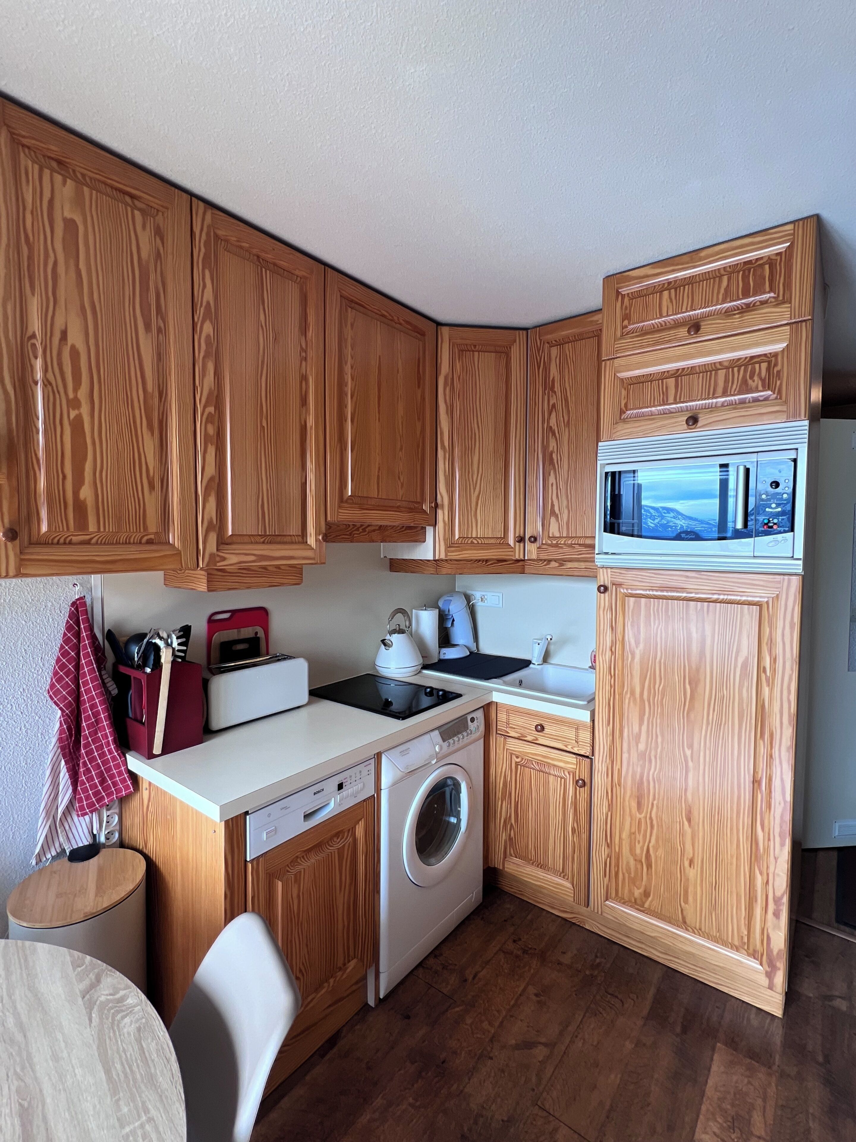 A compact kitchen with wooden cabinets, a microwave, a washing machine, and a toaster.