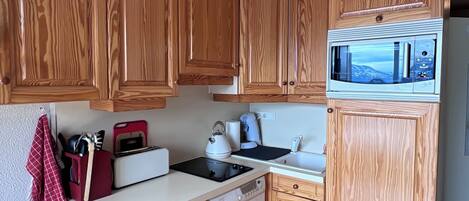 A compact kitchen with wooden cabinets, a microwave, a washing machine, and a toaster.