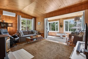 Interior acollidor d'una cabana amb parets de fusta, un sofà, una taula de cafè i una televisió.