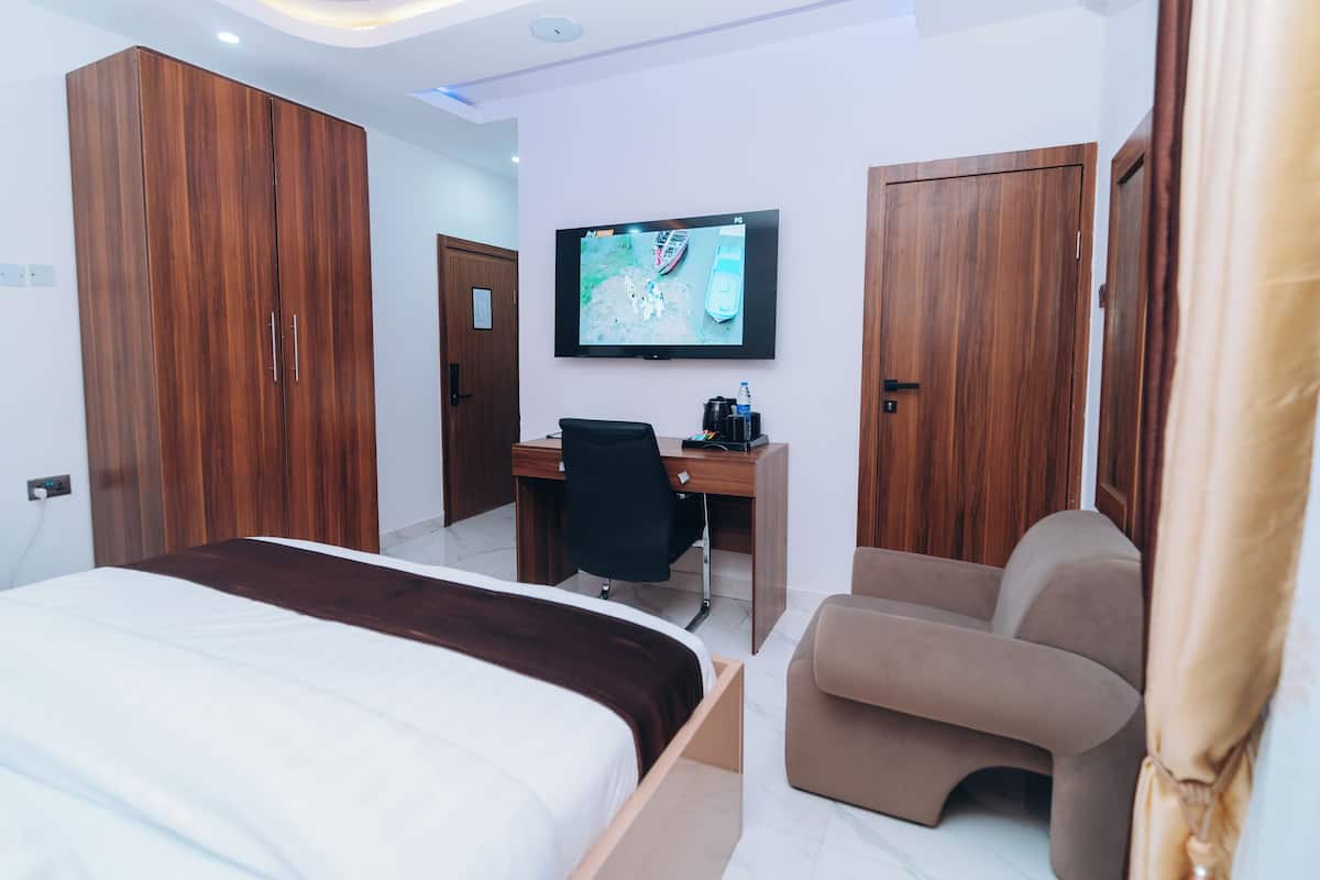 Een hotelkamer met een bed, een bureau, een stoel, een televisie en houten kasten.