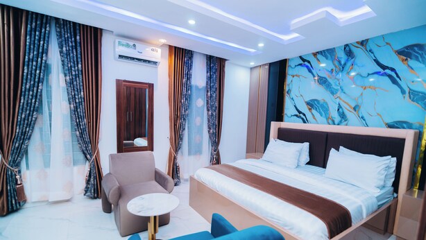 A modern hotel room with a large bed, a sofa, a small round table, and a marble-patterned wall. - VHS VINCHEE SUITES II (Lagos)