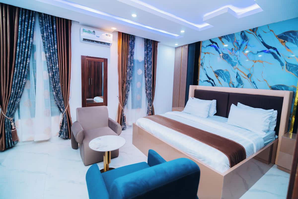 Een moderne hotelkamer met een groot bed, een bank, een klein rond tafeltje en een wand met een marmerprint.