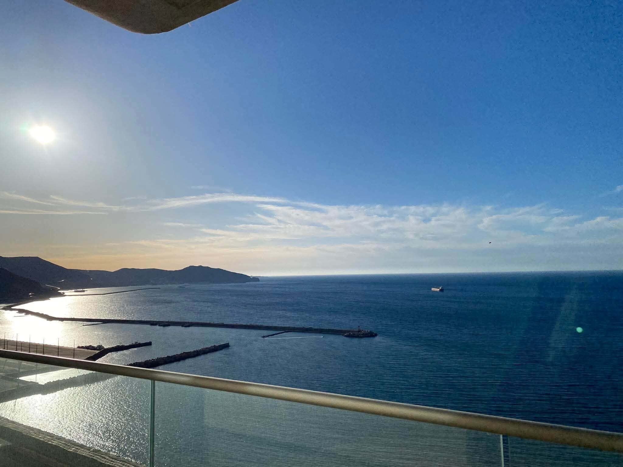 Vista costeira com céu claro, um barco na água e uma terra ao longe.