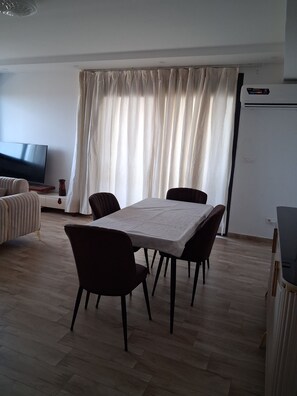 A dining area with a table, chairs, a television, and a window with curtains. - Magnificent sea view apartment (Bir El Djir)