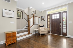 A staircase with wooden railings, a chair, a small table, and a dresser in a hallway with hardwood floors and framed pictures on the walls. - The Experience at ND<>4BR, 4BA <1 mi to ND Stadium (South Bend)