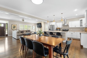 A spacious living area with a wooden dining table, black chairs, a sofa, and a kitchen with white cabinets and stainless steel appliances. - The Experience at ND<>4BR, 4BA <1 mi to ND Stadium (South Bend)