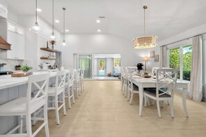 A modern kitchen with white cabinetry, pendant lights, and a dining area with white chairs and a table. - St. Armands Oasis | Pool, Tiki & Putting Green (Sarasota)