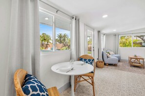 A room with a round table, a sofa, a chair, a small table, and a view of palm trees. - St. Armands Oasis | Pool, Tiki & Putting Green (Sarasota)