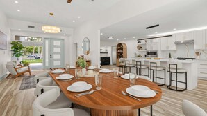 A modern kitchen with white cabinets, a wooden island, and a dining area with white chairs and a wooden table set for six. - St. Armands Circle Luxe 5BR Home with Private Pool (Sarasota)