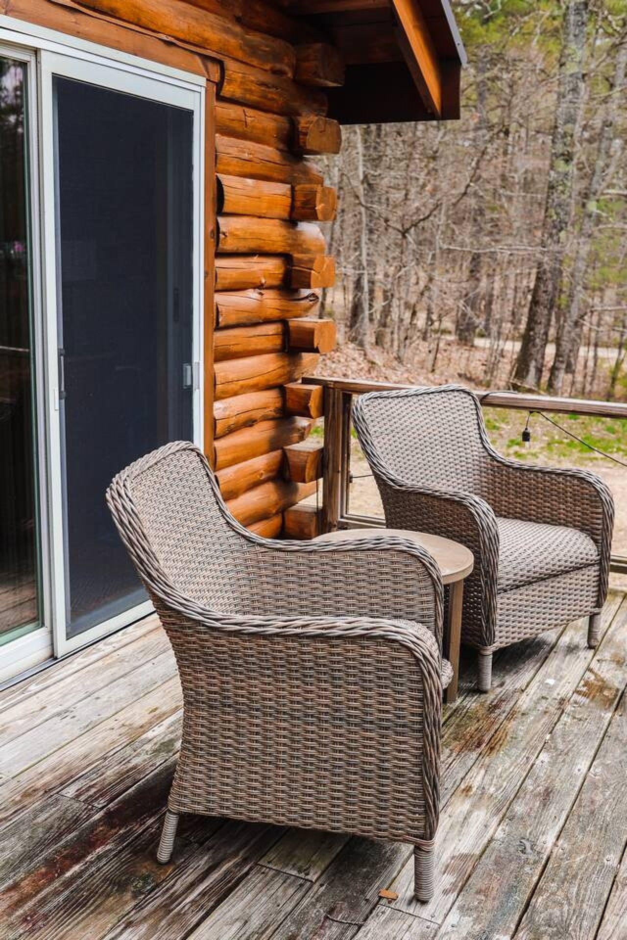 A log cabin with a sliding glass door, two wicker chairs, and a small table on a wooden deck.