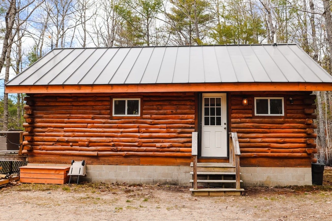 Una cabaña de troncos con techo de metal, una puerta principal y dos ventanas.
