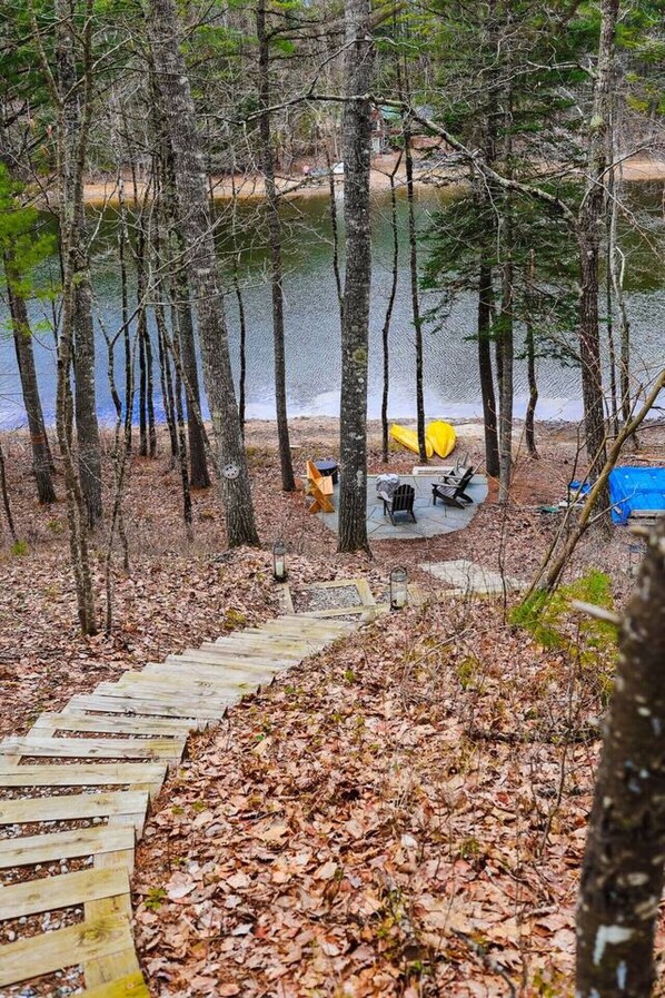 A forested area with a wooden deck leading to a campsite by a lake.