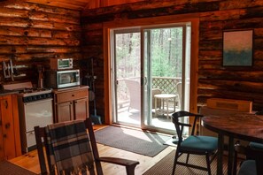 A cabin interior with a kitchen, dining area, and a sliding glass door leading to a deck.