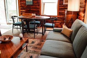 A cozy room with a wooden log wall, a round dining table with chairs, a sofa, and a lamp. - Long Pond Cabin Retreat (Denmark)
